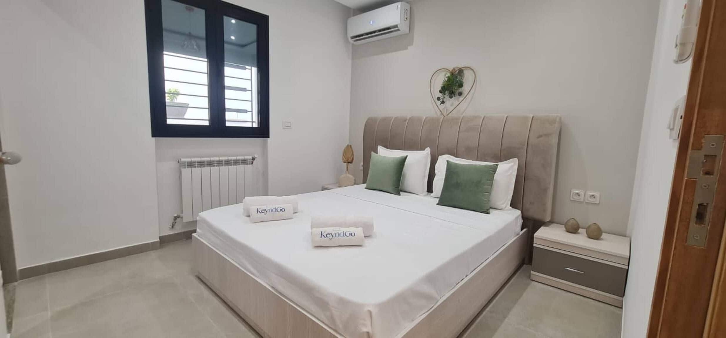 Une chambre à coucher comprenant un lit, une fenêtre, un appareil de climatisation, un radiateur, une table de chevet et une commode.