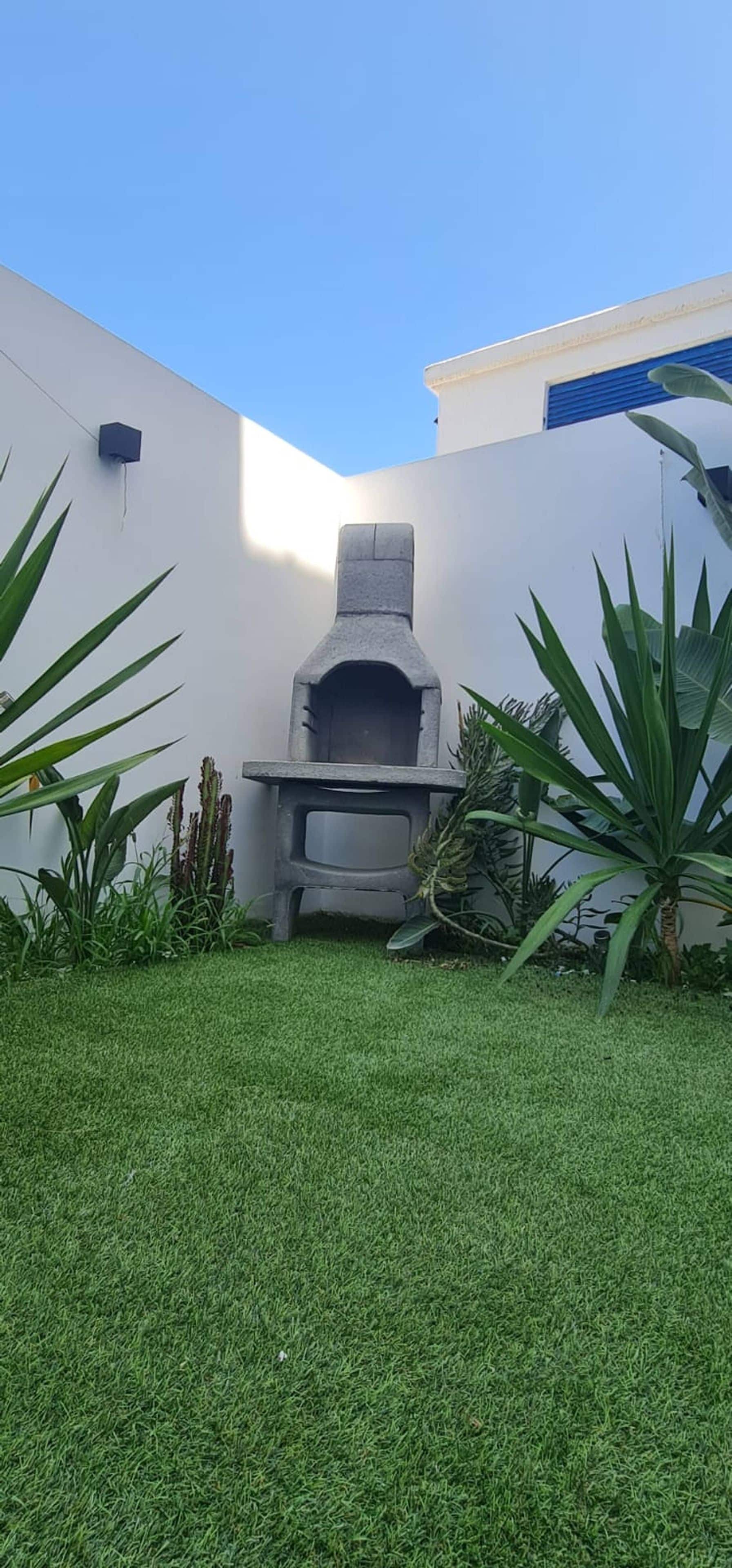 A stone-built outdoor oven in a grassy area with white walls and tropical plants.