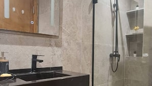 Un baño con tocador oscuro, espejo, cabina de ducha y suelo de baldosas.