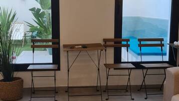 Una sala moderna con vista a la piscina, dos mesas de madera, una mesa baja blanca y un sofá.