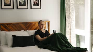 En person sidder på en seng med en smartphone, et træsenggærde og billeder i rammer på væggen.