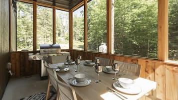 En træhytte med et spisebord til fire, grill og udsigt til en skov.