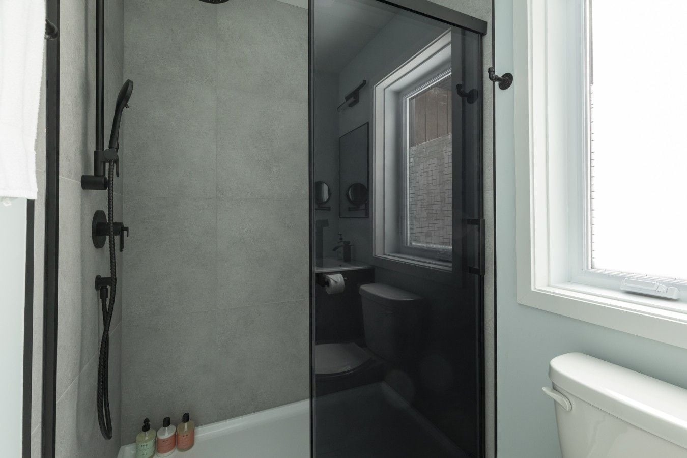 Ein Badezimmer mit Duschkabine aus Glas, Toilette, Waschbecken und Fenster.