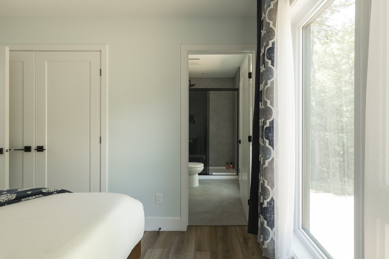 A bedroom with a bed, a door, and a window with curtains.