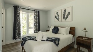 Une chambre à coucher avec un grand lit, deux tables de chevet, une fenêtre avec des rideaux et deux œuvres d’art en plumes accrochées au mur.
