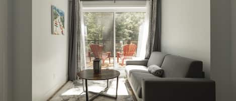 A living room with a grey sofa, a round coffee table, and a view of an outdoor patio with red chairs.