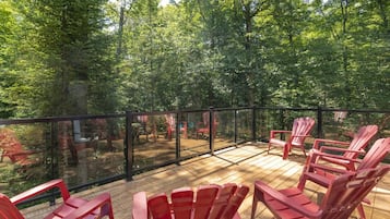 A deck with red chairs and a glass railing overlooking a forested area.