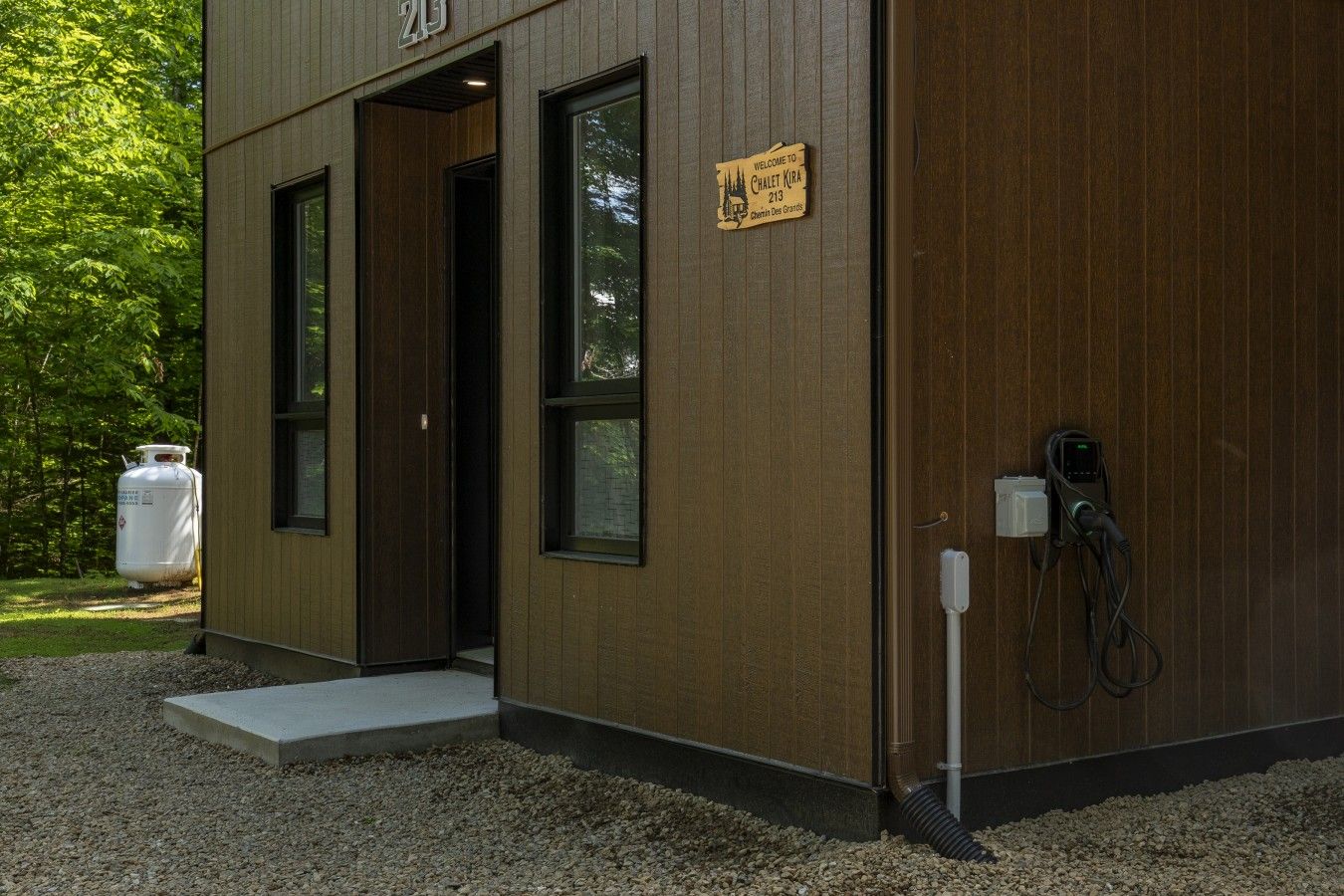 Un bâtiment moderne avec une façade en bois, une enseigne d’accueil et une borne de recharge.