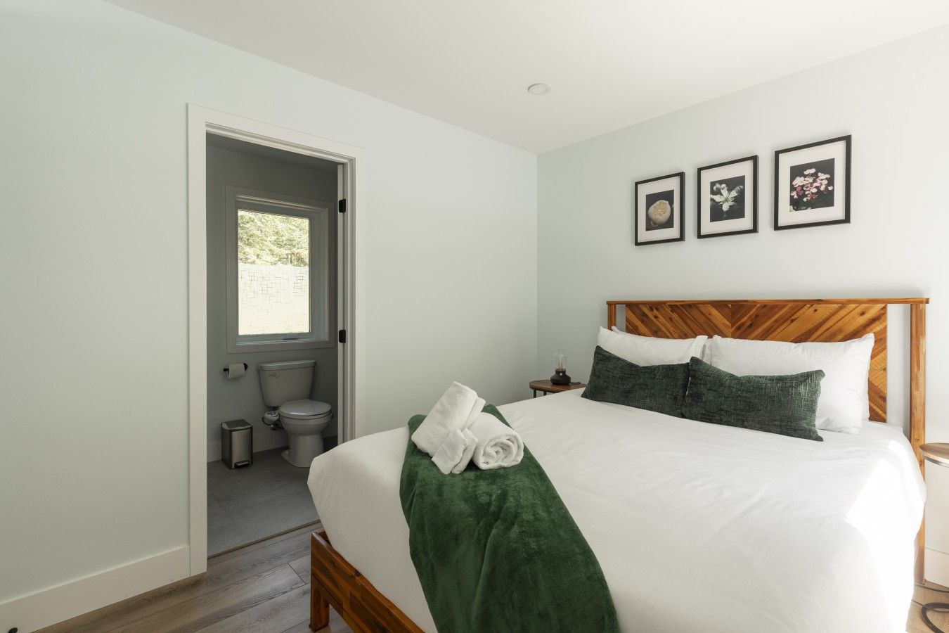 A hotel room with a bed, a wooden headboard, a window, a door, and a toilet.