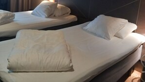 A hotel room with two beds, each with white linens and pillows, a bedside table with a lamp, and a window with curtains. - Vrbo Property (Cannes)