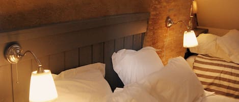 A hotel room with a bed, two bedside lamps, and a brick wall.