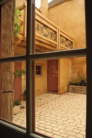 A courtyard with a tiled floor, a wooden door, and a window with a decorative metal railing. - Historic House in the Heart of Sancerre – Wines, Restaurants, and the Village Within Walking Distance (Sancerre)