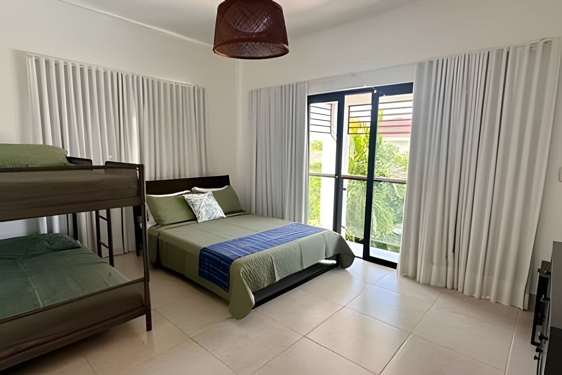 Une chambre d’hôtel avec un lit superposé, un lit simple, une grande fenêtre avec des rideaux et un luminaire au plafond.