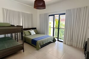 Quarto de hotel com cama beliche, uma cama de solteiro, uma janela grande com cortinas e luminária no teto.