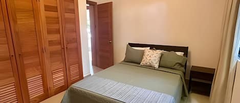 A bedroom with a bed, wooden wardrobe, and a door leading to another room.
