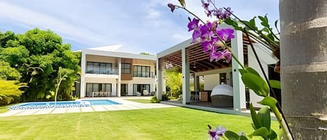 A modern two-story house with a covered patio, a swimming pool, and lush greenery.