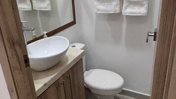A small bathroom with a sink, toilet, and a mirror. There are two towels hanging on a rack.