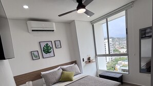 Ein modernes Schlafzimmer mit Bett, Deckenventilator, Klimaanlage und großem Fenster mit Blick auf die Stadt.