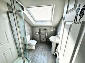 Een kleine badkamer met een dakraam, toilet, wastafel en douchehoek.