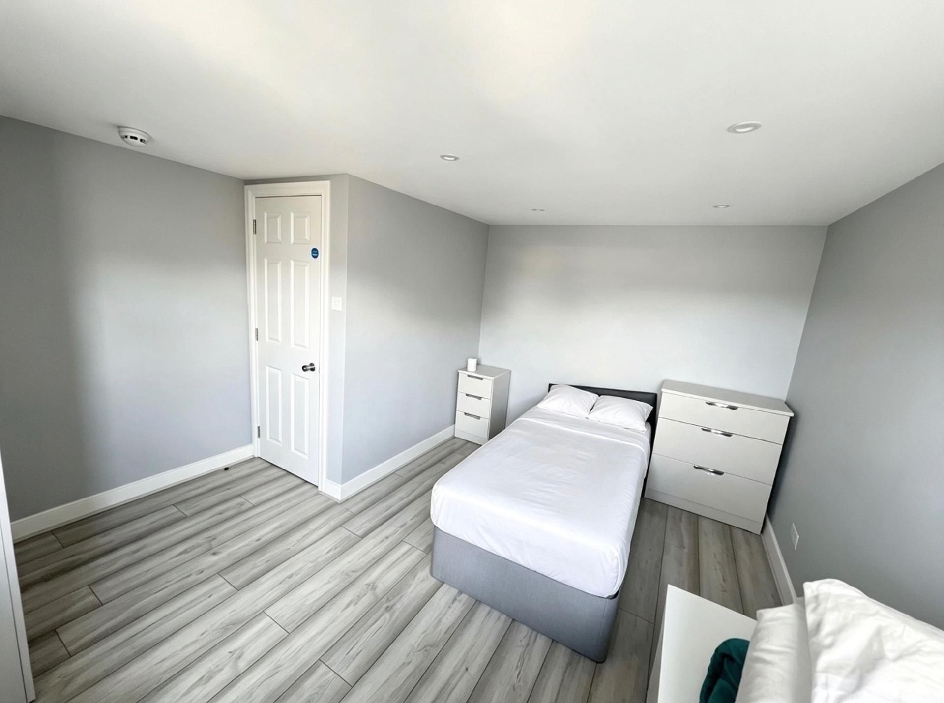Een slaapkamer met een bed, nachtkastje, kledingkast en een deur.