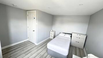 Een slaapkamer met een bed, nachtkastje, kledingkast en een deur.