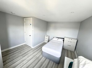 A bedroom with a bed, a nightstand, a dresser, and a door.