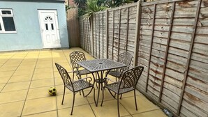 A patio with a table and chairs, a door, and a wooden fence. - South East London 5-bed House, Sleeps 7 Foresthill (London)
