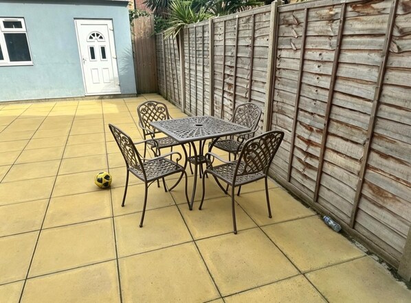A patio with a table and chairs, a door, and a wooden fence.