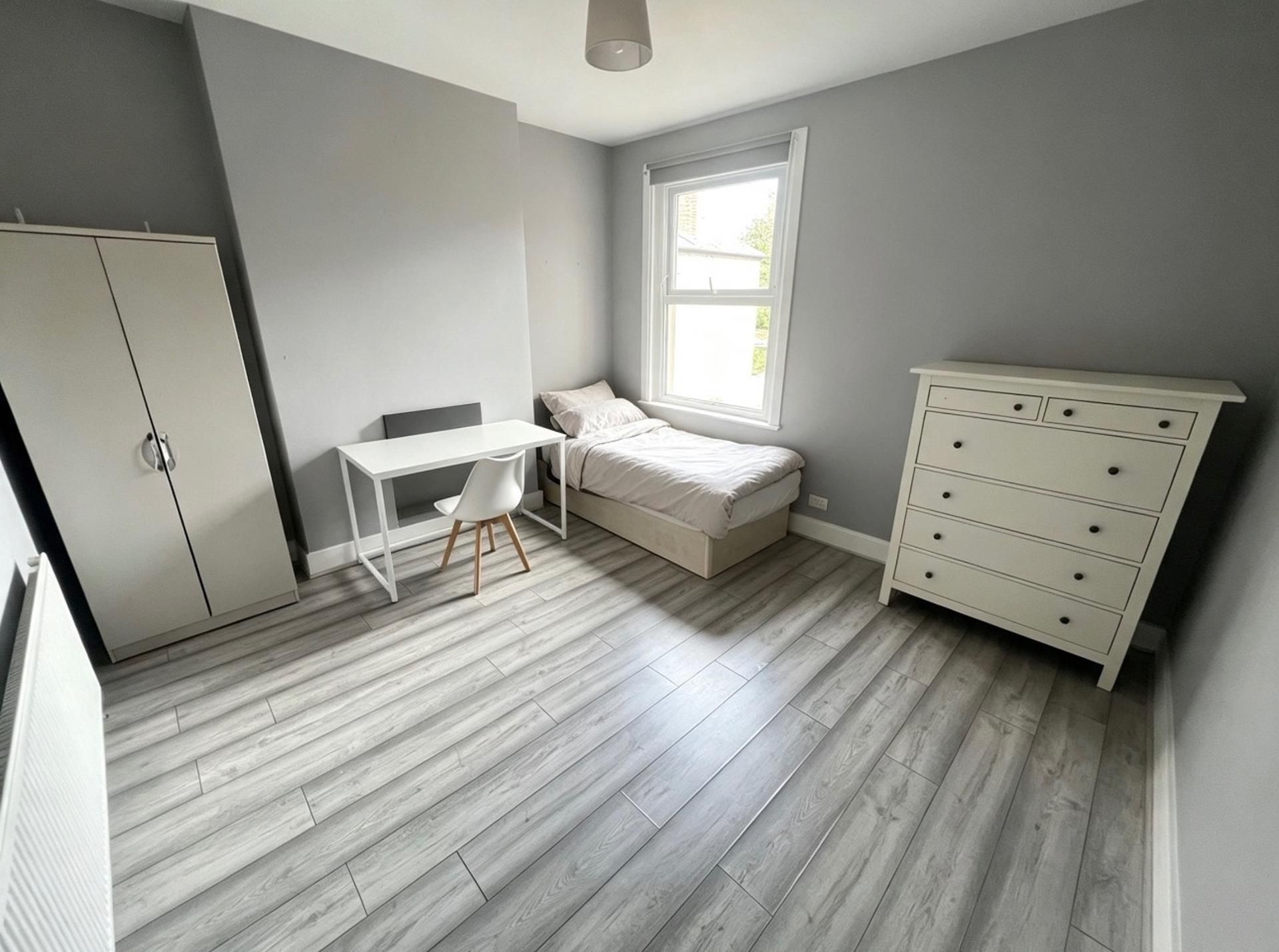 Ein Schlafzimmer mit einem Bett, einem Schreibtisch, einem Stuhl, einer Kommode und einem Kleiderschrank.