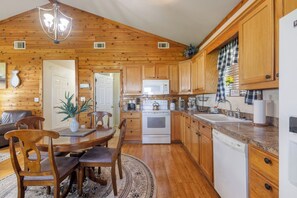 A wooden cabin interior with a dining area, kitchen, and a ceiling light fixture.