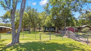 A fenced outdoor area with trees, a small building, and a red barn. - HunnyBear Hideout on Cedar Creek Lake (Eustace)