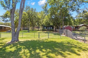 A fenced outdoor area with trees, a small building, and a red barn. - HunnyBear Hideout on Cedar Creek Lake (Eustace)