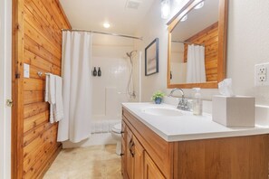 Une salle de bain avec des murs recouverts de panneaux en bois, un lavabo blanc, un miroir et un espace douche.
