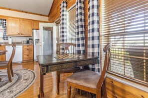 A wooden dining table with chairs, a chessboard, and a window with blinds.