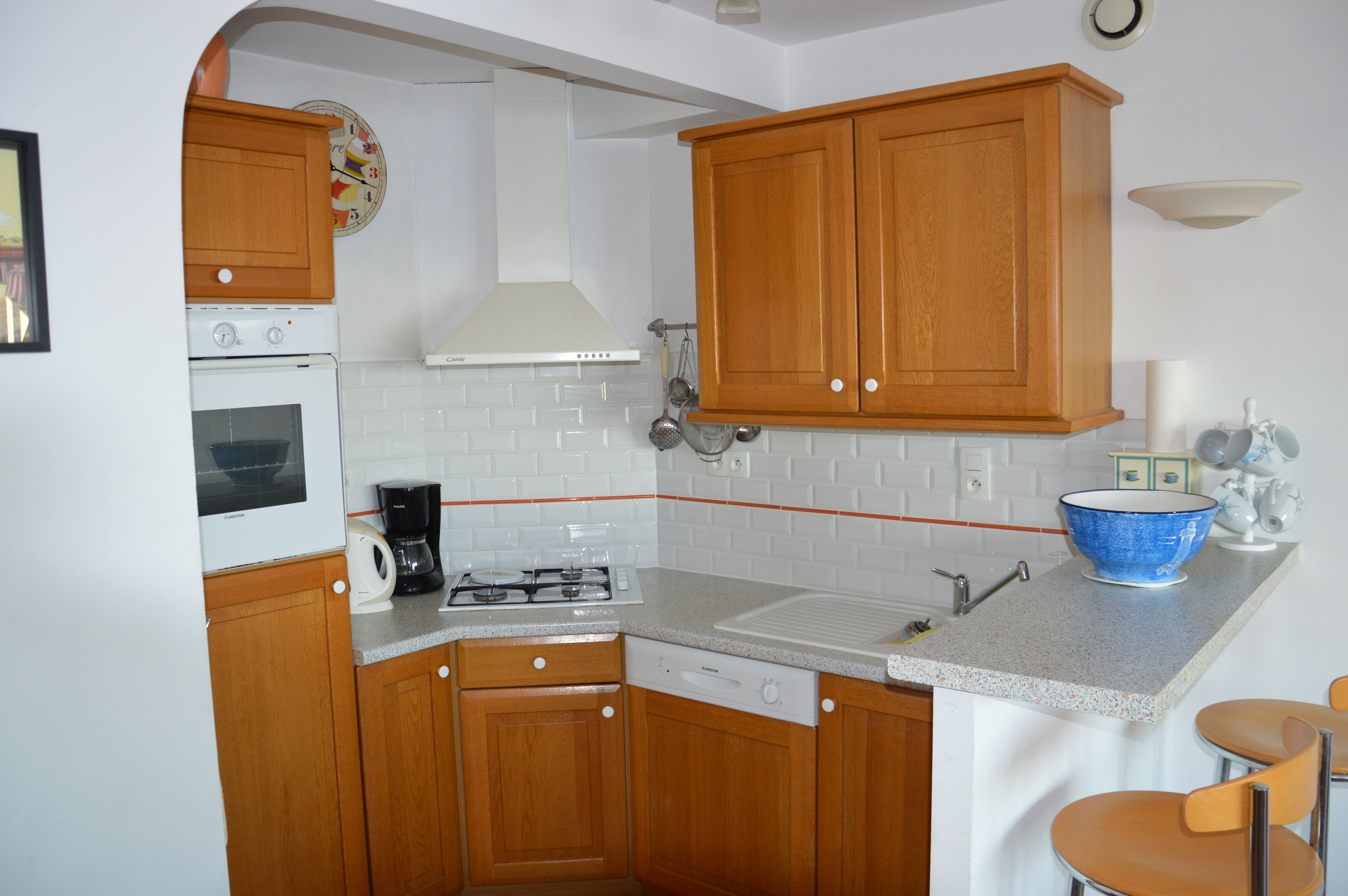 Une cuisine compacte avec des meubles de rangement en bois, une cuisinière à gaz, une machine à café et un évier.