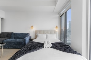 Camera d'hotel moderna con un ampio letto, una poltrona e vista sulla città.