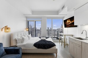 Camera da letto moderna con vista sulla città, un letto grande, una TV e un angolo cottura.