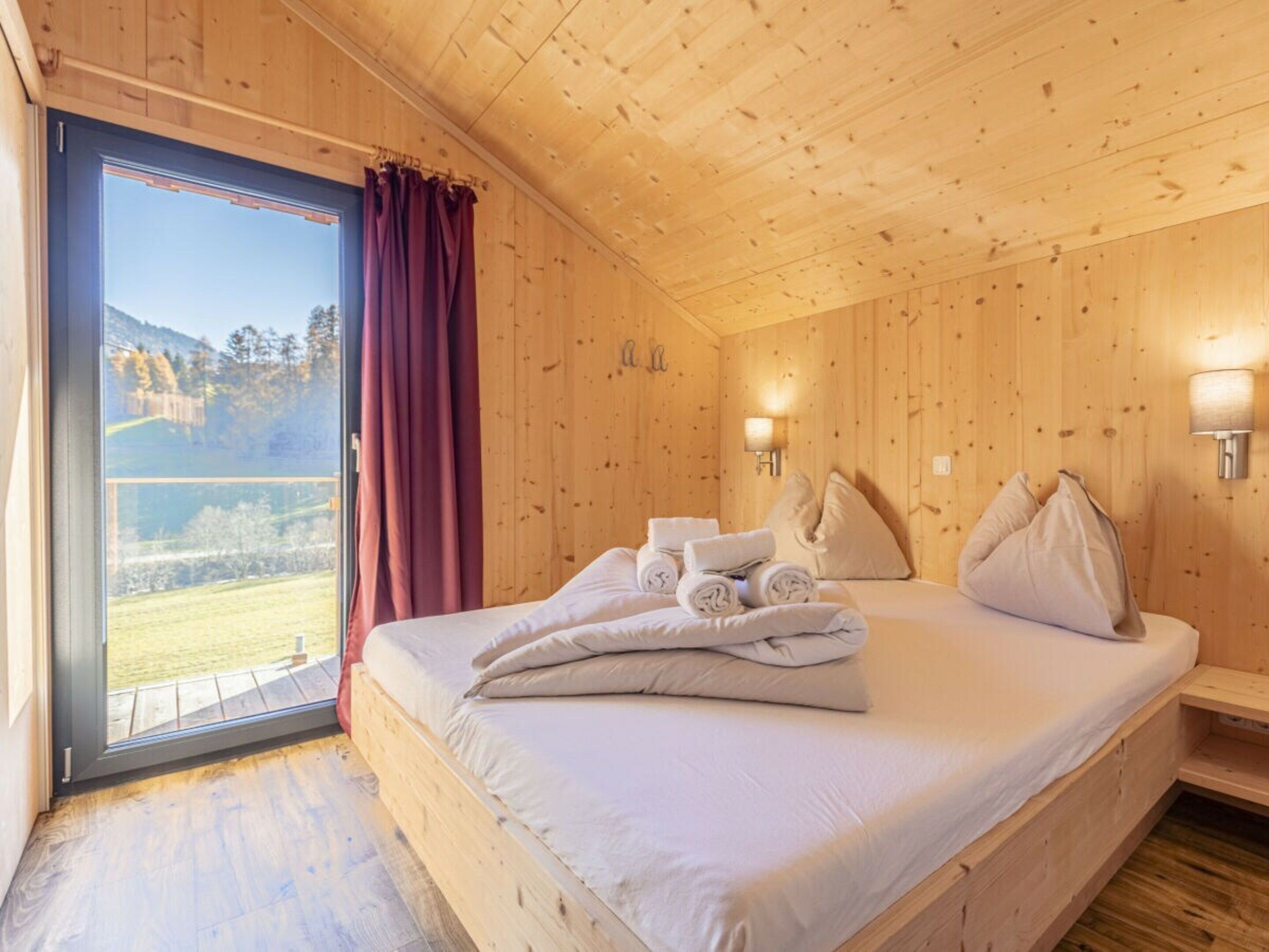 Una habitación de madera con una cama, una ventana con cortinas y vista a un paisaje.