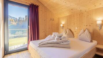 Una habitación de madera con una cama, una ventana con cortinas y vista a un paisaje.