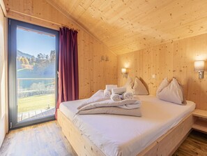 Ein Zimmer mit Holzboden, einem Bett, einem Fenster mit Vorhängen und Blick auf eine Landschaft.