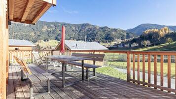 Una terraza de madera con una mesa y bancos, con vistas a un paisaje montañoso.