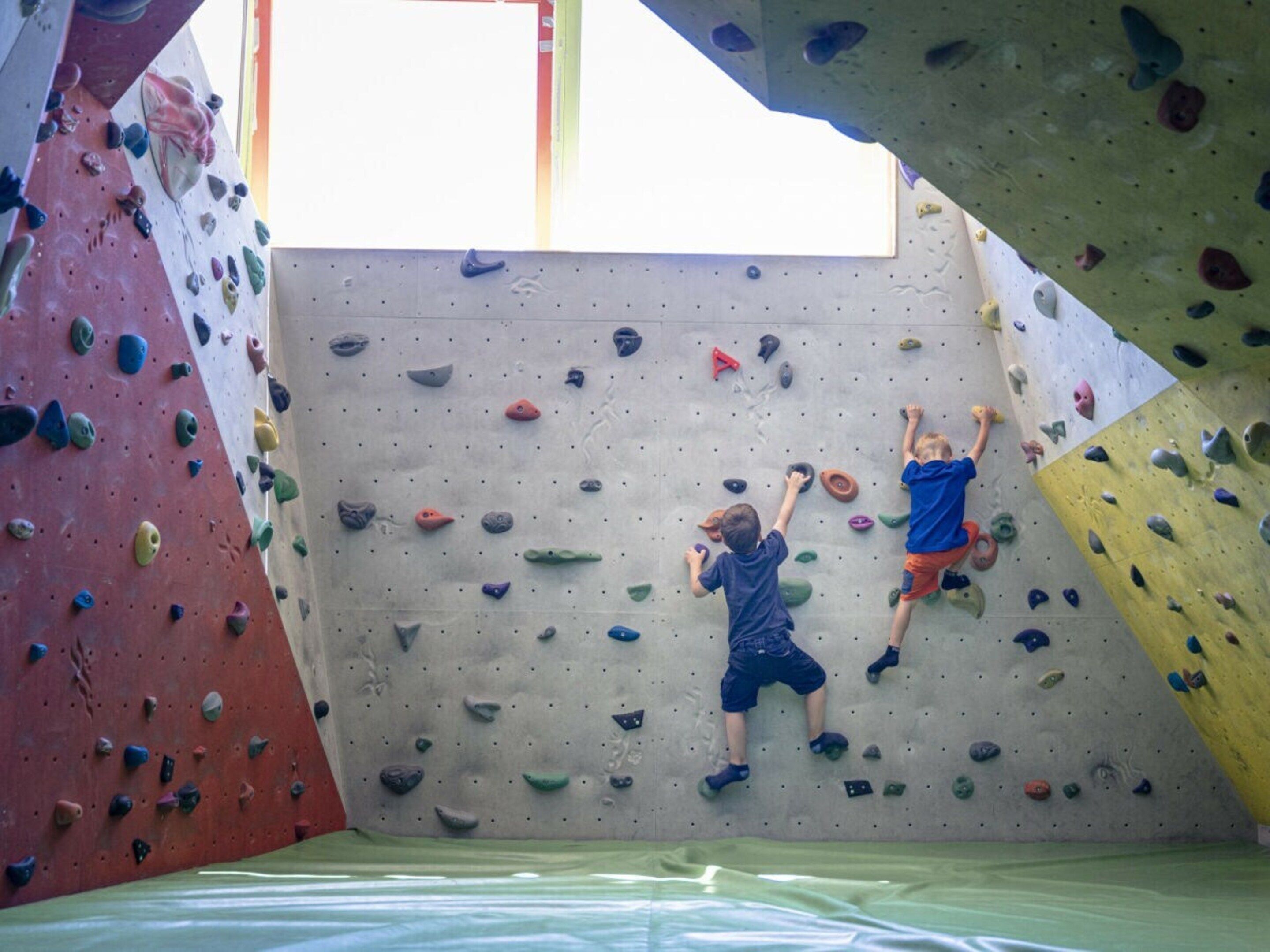 Una pared de escalada con varios puntos de agarre y dos niños escalando.