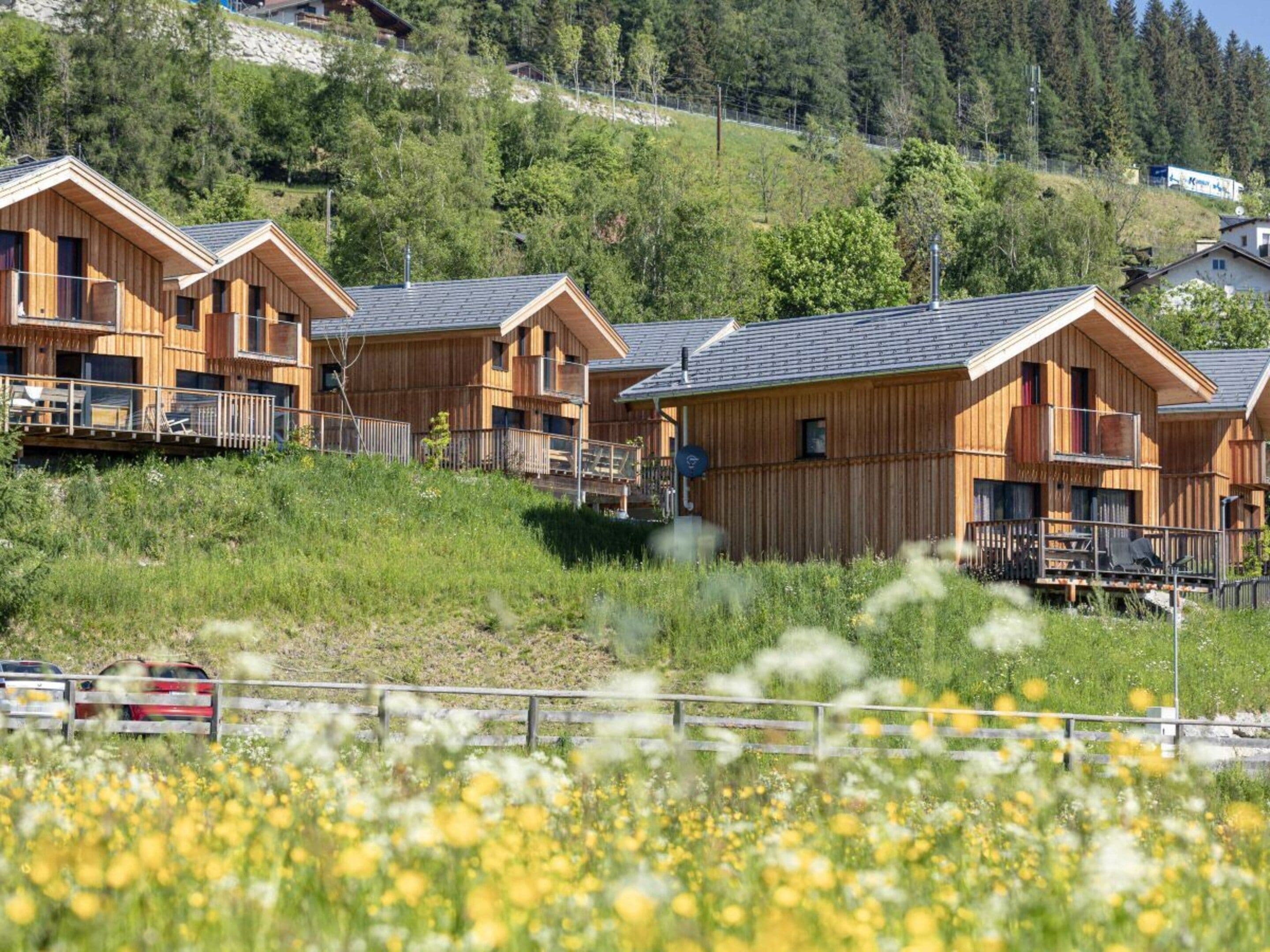 Una hilera de cabañas de madera con balcones, frente a una ladera y un cielo despejado.