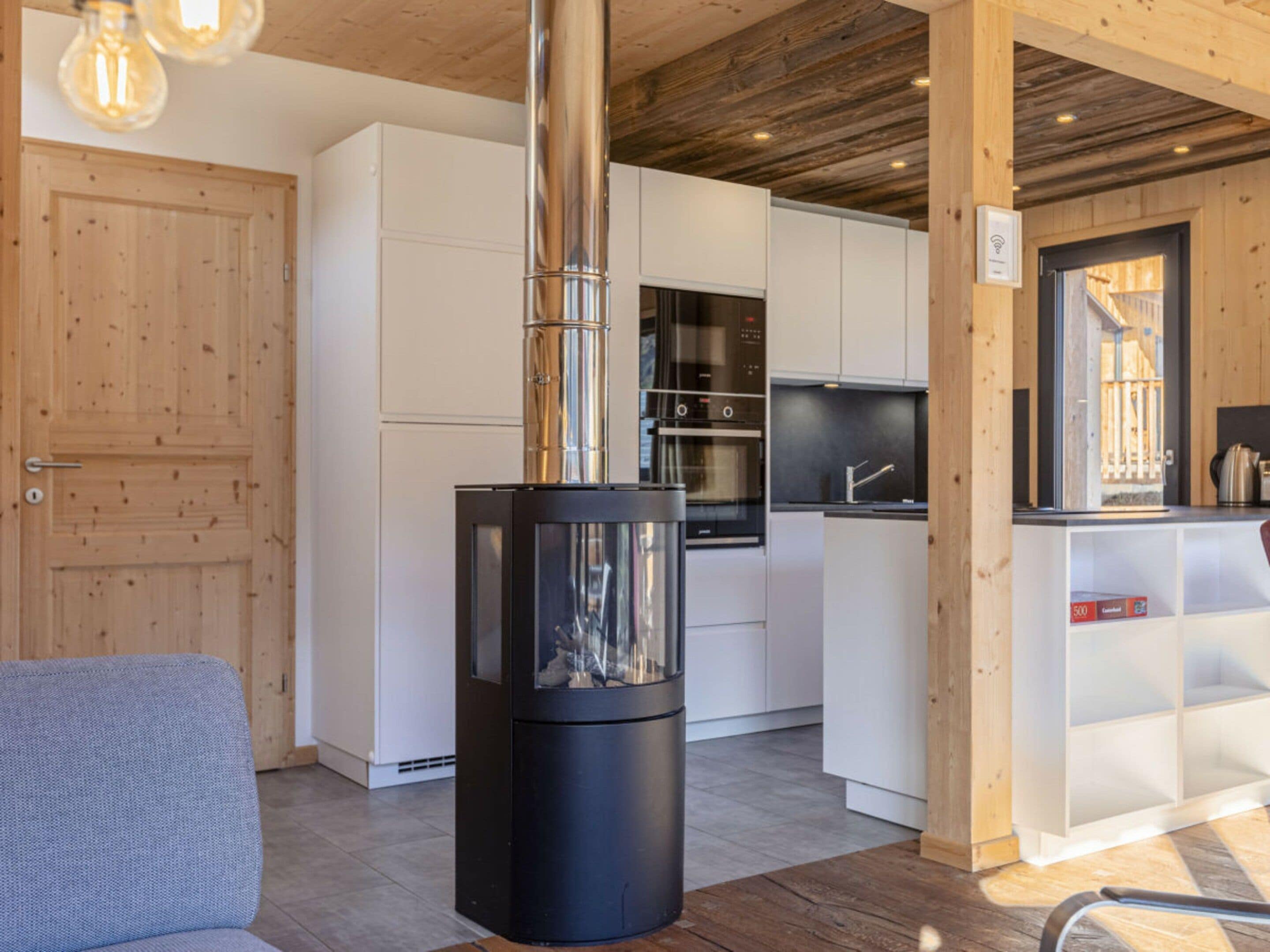 Una cocina moderna con un horno de leña central, armarios blancos y techo de madera.
