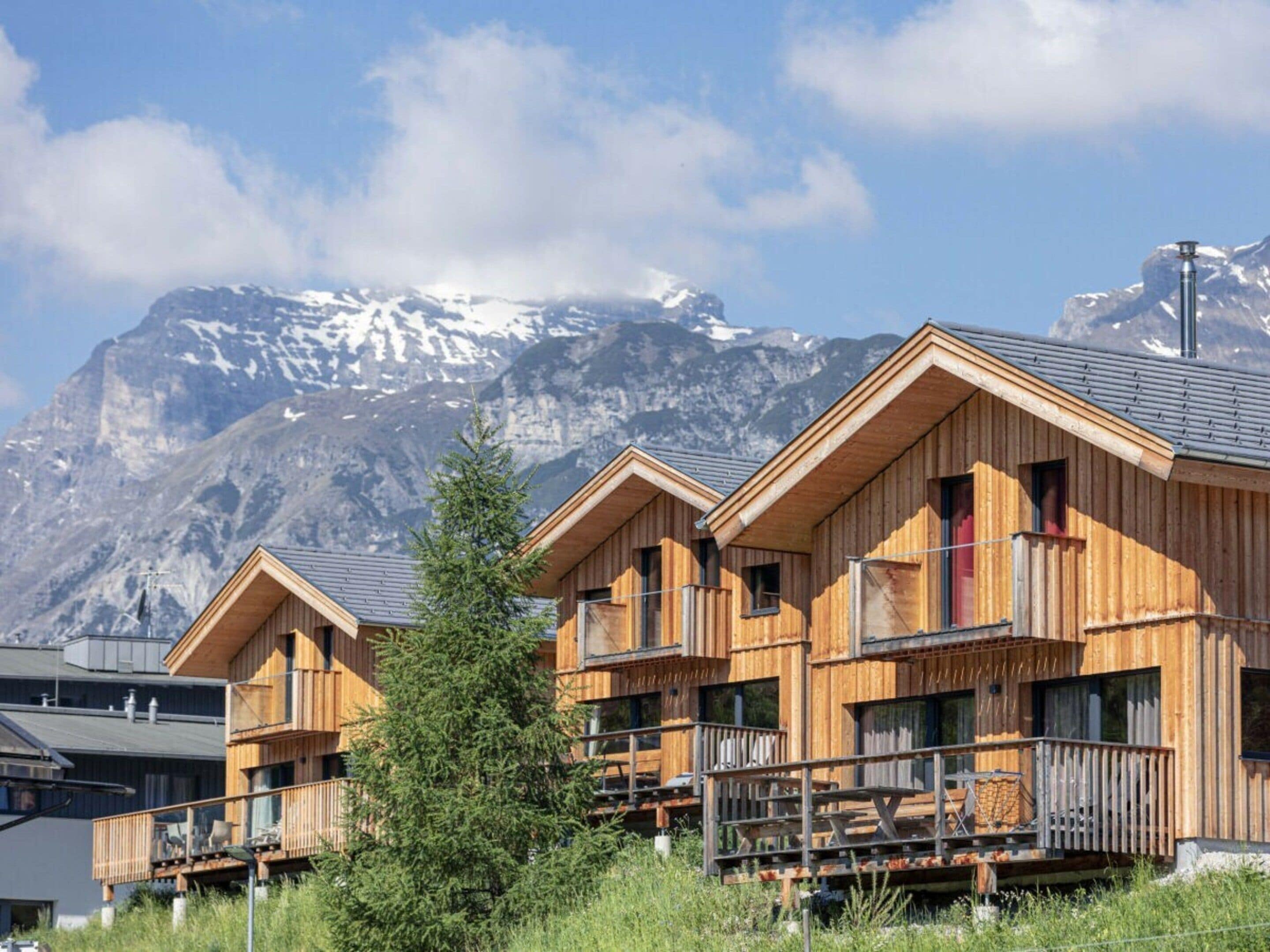 A wooden chalet with balconies, set against a backdrop of snow-capped mountains.