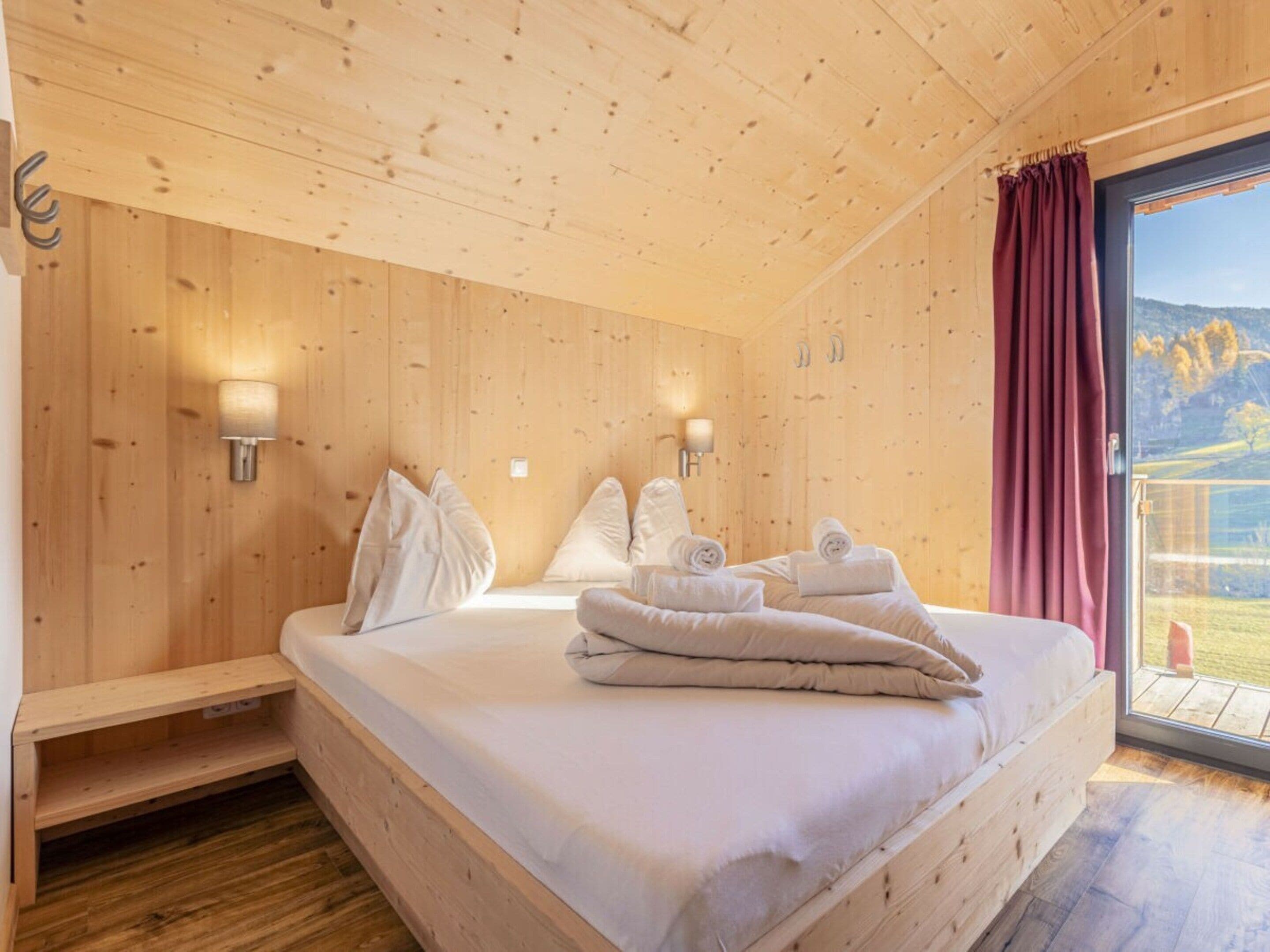 Een kamer met houten vloer, een bed, twee wandlampen en een raam met uitzicht.