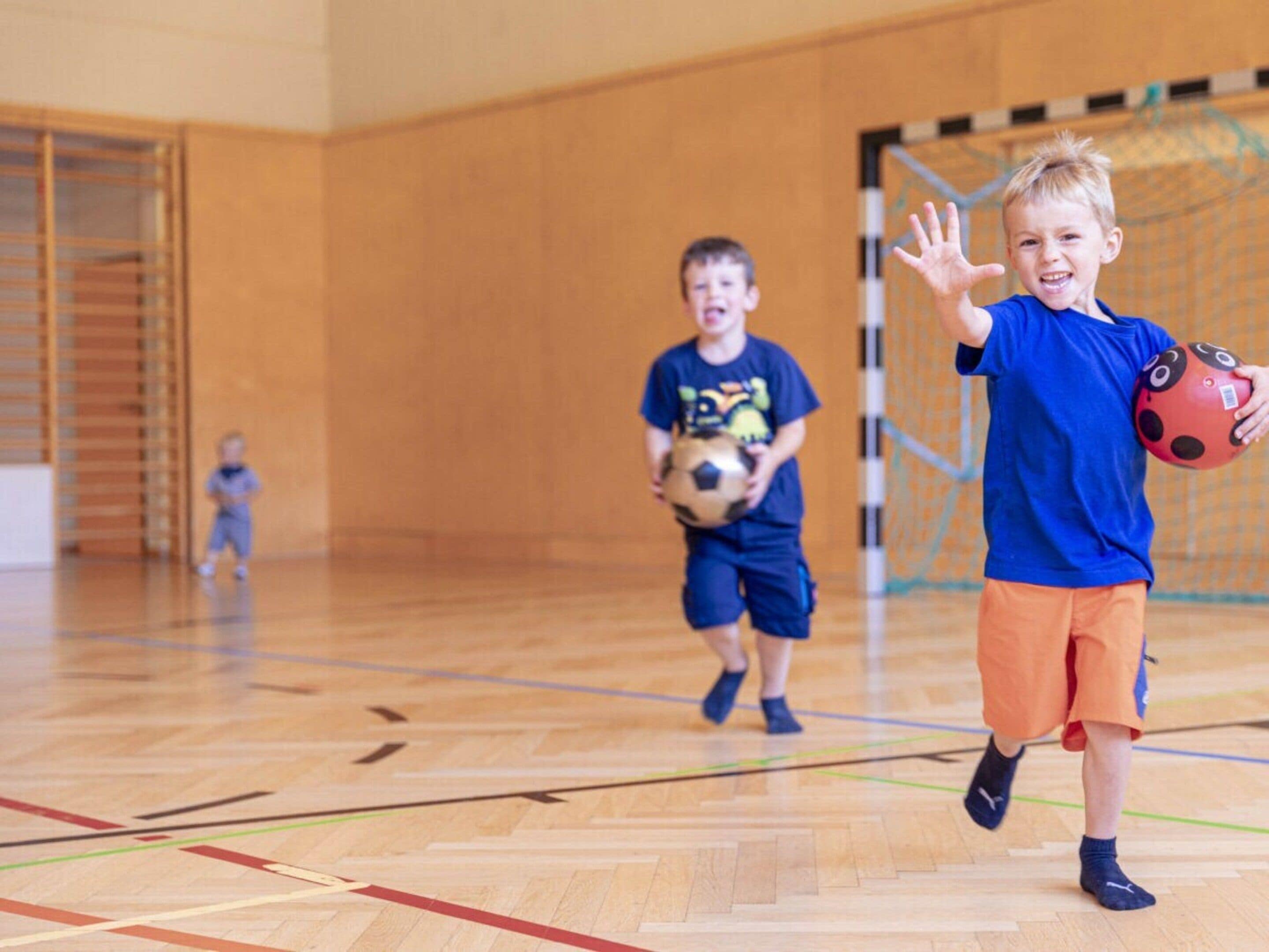 Un gimnasio con una cancha de baloncesto, un aro y niños jugando.