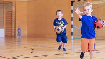 Un gimnasio con una cancha de baloncesto, un aro y niños jugando.