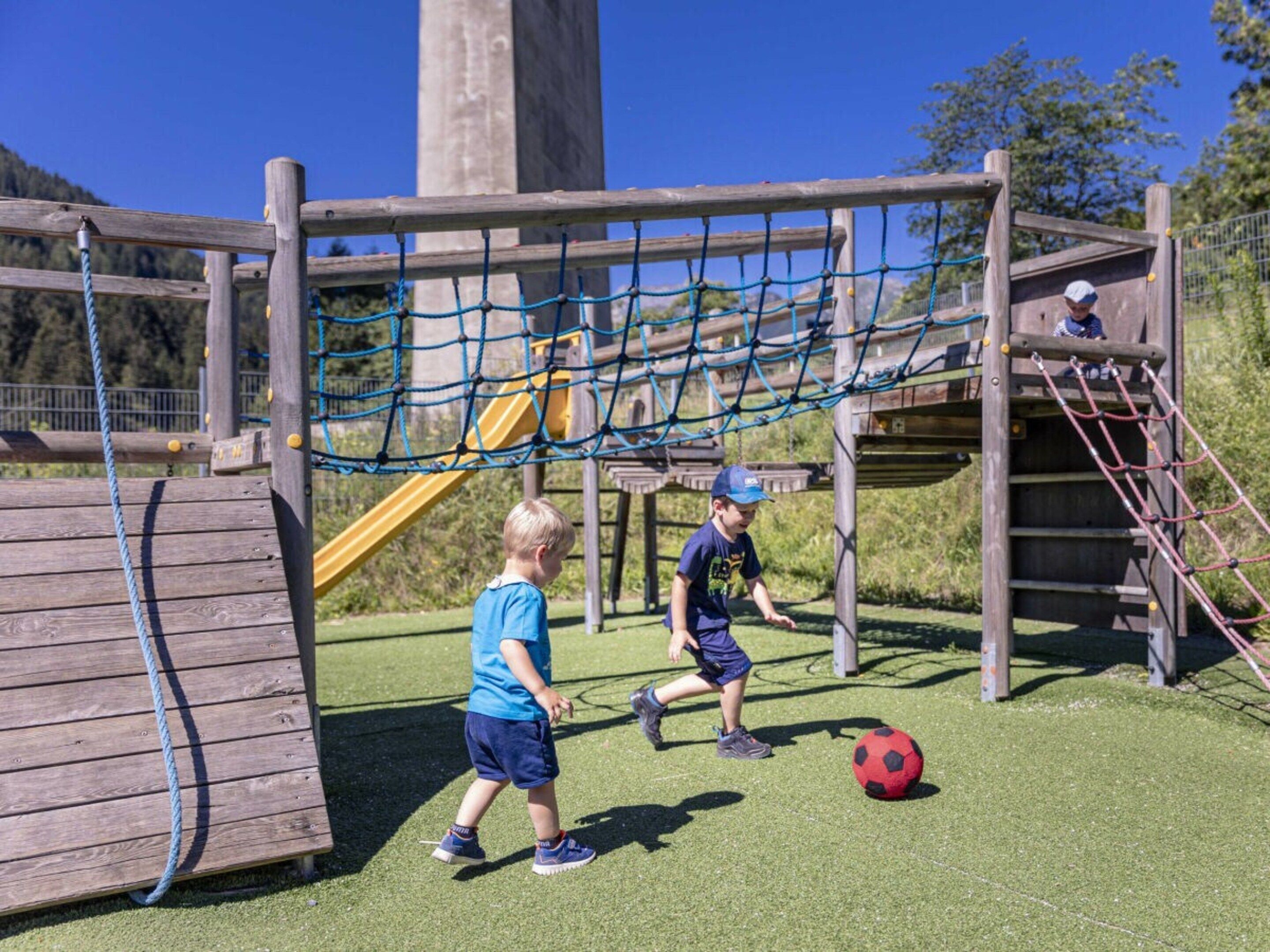 Un parque infantil con un puente de cuerda, un tobogán y una estructura para escalar.