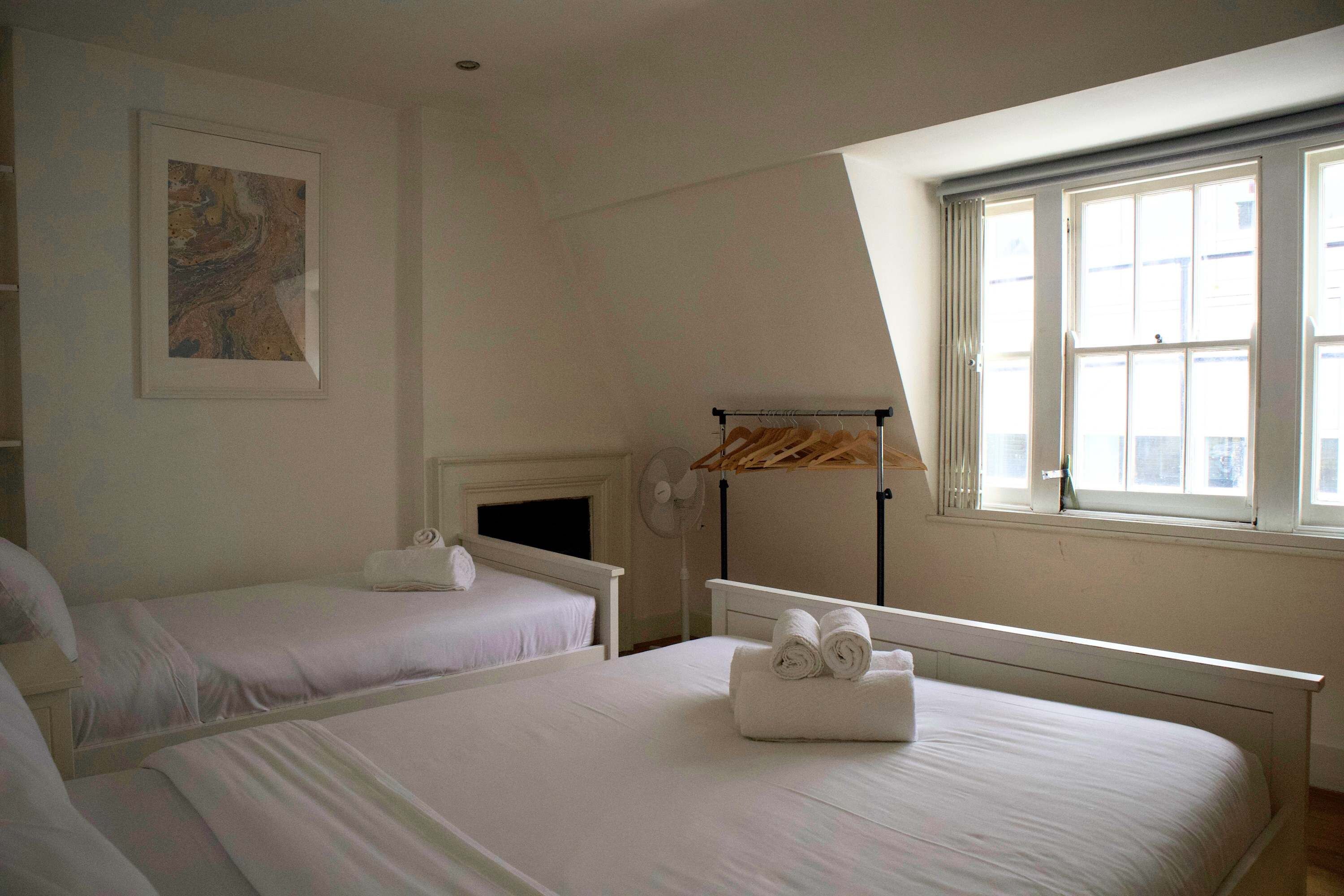 Une chambre d’hôtel avec deux lits, un ventilateur de plafond, une fenêtre avec des rideaux et un tableau au mur.